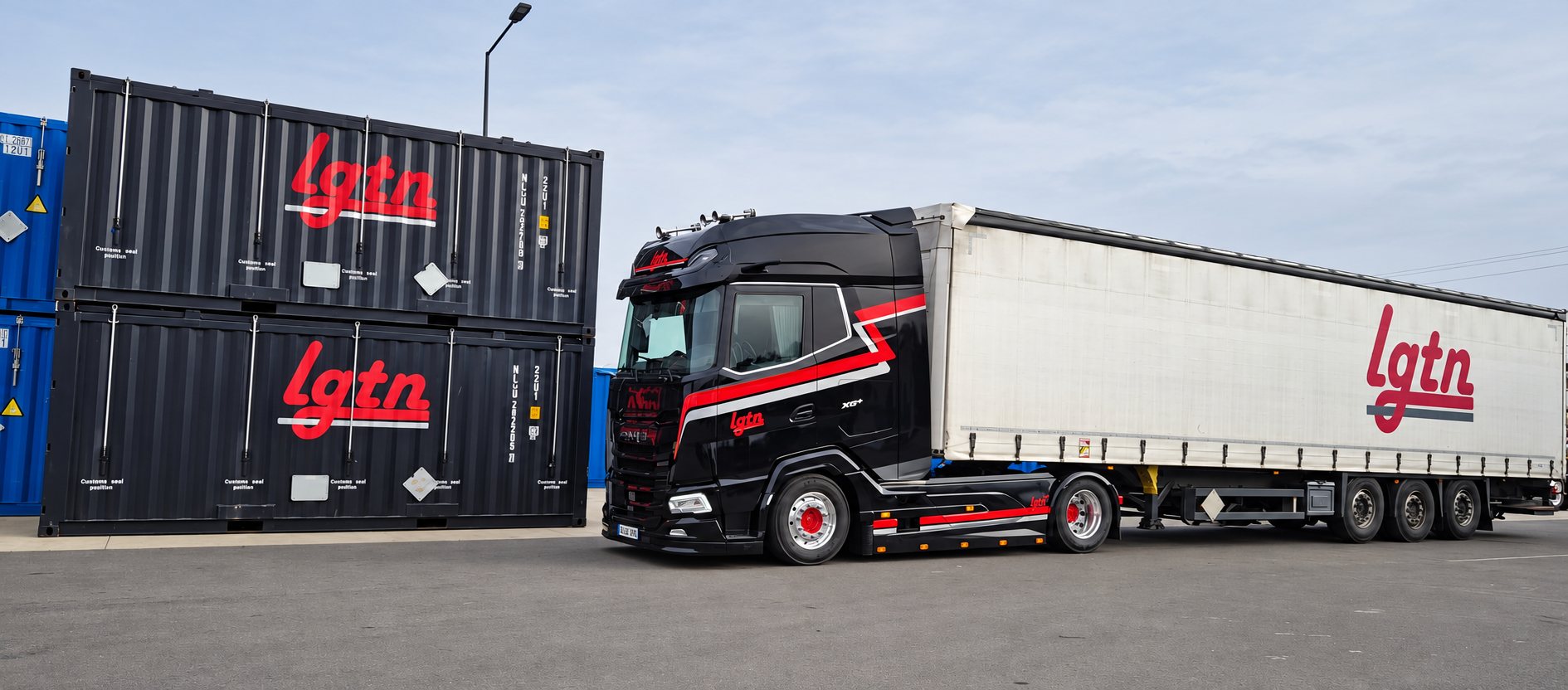 Un camion tracteur noir aux bandes rouges attelé à une remorque à bâches blanche est garé devant deux conteneurs noirs empilés portant le logo lgtn.