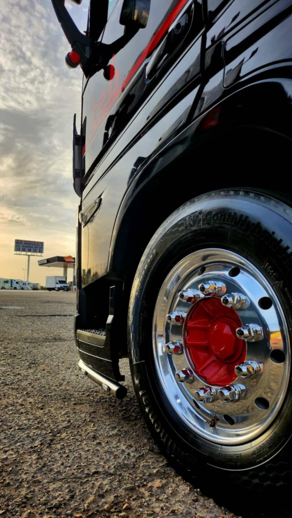 Gros plan sur la roue en aluminium poli à moyeu rouge d'un camion noir brillant, garé sur un parking au coucher du soleil.